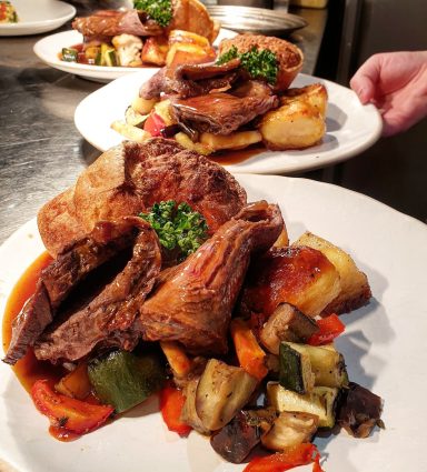 Roast meat with vegetables and potatoes, garnished with herbs on a white plate.