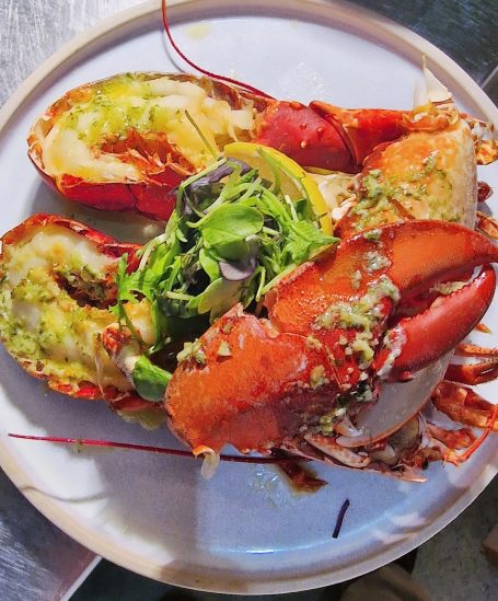 Lobster halves served with a garnish of mixed greens on a white plate.